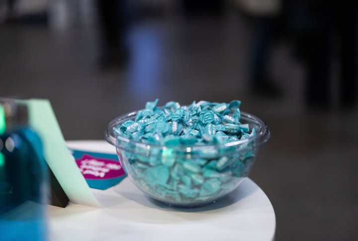 Glasskål fylld med turkosa karameller på ett bord.